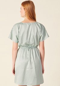 Vestido impreso con patrón hexagonal verde, mangas cortas, cintura elástica y una tela suave y ligera. La vista trasera muestra un detalle fruncido.