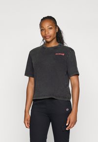 Sort kortærmet t-shirt i blødt stof med et rødt "CHAMPION" logo på venstre bryst. Casual, afslappet pasform med rund halsudskæring.