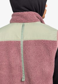 Fleecepullover mit einer sanft rosa Außenseite und einem mintgrünen oberen Rückenteil. Er hat eine strukturierte Oberfläche und einen vertikalen Akzent an der Naht.