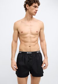 Čierne boxerky so zapínaním na gombíky, s elastickým pásom s bielym logom "BOSS". Hladká tkanina s priliehavým strihom.