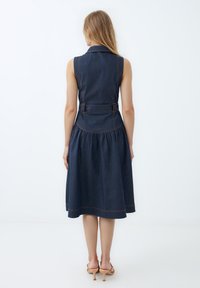 Ärmelloses Jeanskleid in Dunkelblau mit taillierter Oberseite, ausgestellt Rock und orangefarbener Naht. Hat eine definierte Taille und einen Kragen.