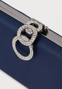 Μπλέ τσάντα χιαστί με κομψή σατινέ υφή, μεταλλικά αξεσουάρ και διακοσμητικό ασημένιο κούμπωμα με διασυνδεδεμένους δακτυλίους καλυμμένους με στρας.