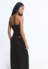 Czarny gorset bez ramiączek o błyszczącej fakturze, zestawiony z luźnymi, czarnymi spodniami o szerokich nogawkach. Gorset ma dopasowany krój podkreślający sylwetkę.