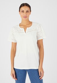 Top bianco a maniche corte con ricami ad occhio di pernice sulle spalle, scollatura a chiave e vestibilità relaxed. Texture liscia con design minimale.