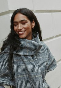 Hall ja must ruuduline sall pehmest, tekstuuriga materjalist, laia langeva disainiga ja mustri ääres õrnad tan tooniga aktsendid.