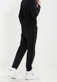 Sort sweatshirt med lange ærmer, kombineret med løse sorte jeans. Fodtøjet er hvide FILA-sneakers med kraftige såler og logo.