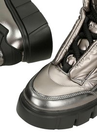 Masywne buty na platformie z metalicznie srebrną cholewką, czarną wyściełaną kołnierzową częścią, grubymi czarnymi sznurówkami i grubą czarną ryflowaną podeszwą.