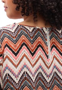 Πολύχρωμο ύφασμα με ζιγκ-ζαγκ σχέδια σε σκουριά, ροζ, μαύρο και μπλε; διαθέτει φερμουάρ στην πλάτη και υφή επιφάνειας.