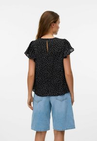 Svart t-shirt med korta ärmar och vita prickar, med en nyckelhålskärning bak, kombinerad med ljusblå denimshorts. Lätt, texturerad tyg.
