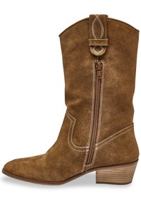 Botte de cowboy en daim marron avec une fermeture éclair sur le côté, à bout pointu et talon empilé. Présente des coutures blanches et une sangle décorative en haut.