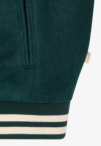 Tume roheline villane jopevarrukas, ribitud mansetiga, millel on kaks koorevalget triipu ja väike beež kangasilt.