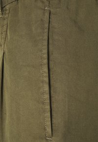 Tissu en mélange de coton vert olive avec une texture lisse, présentant une poche latérale avec des détails de couture visibles.