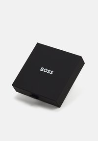 Juodas pristatymo dėžutė pagaminta iš tvirto medžiagos su matinio paviršiaus apdaila, ant viršaus puikuojasi sidabrinėmis raidėmis užrašas "BOSS" ir traukimo juostelė.