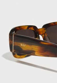 Gafas de sol de carey con lentes oscuros, que cuentan con un marco cuadrado grueso y un logotipo acentuado en dorado "R.S.F." en la patilla.