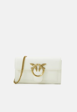 White leather wallet featuring a gold-tone bird emblem with a circular ring. It has a chain strap and a flap closure. Smooth texture.