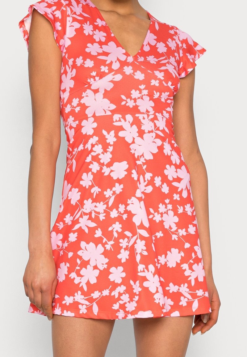 Robe florale avec un décolleté en V, manches courtes volantes, en corail avec des fleurs roses. Tissu lisse, corsage ajusté, jupe évasée.