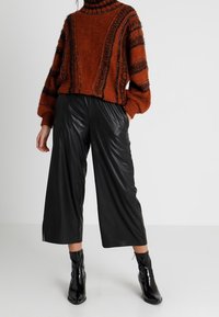 Suéter de punto color óxido con rayas texturizadas, combinado con pantalones de piernas anchas de cuero sintético negro. Botines negros completan el atuendo.