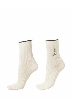 Paire de chaussettes blanches côtelées montant jusqu'à mi-mollet, avec un bord sombre en haut et un petit emblème noir avec du texte sur le côté.