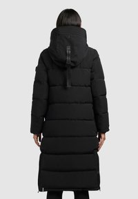 Lange zwarte gewatteerde jas met capuchon, voorzien van een quilted ontwerp, ritszakken aan de zijkant en een logo accent op de achterkant van de kraag.