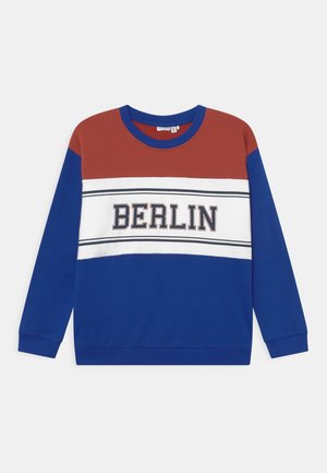Sweatshirt med blå ærmer og bund, rustfarvet øvre bryst, hvid stribe tværs over brystet med teksten "BERLIN" i fede bogstaver.
