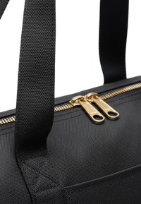 Primo piano di una borsa in tessuto nero con due tirazip dorati e una larga tracolla nera cucita alla borsa.