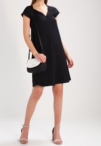 Černé šaty s výstřihem do V a krátkým rukávem, s těsným korzetem a volnou sukní. Doplňují je černobílá crossbody kabelka a světlé šedé sandály na podpatku.