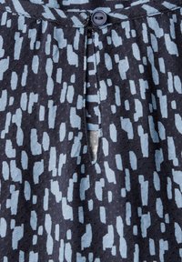 Tessuto blu e navy con motivo a forma irregolare, dotato di chiusura con bottone e di un piccolo aperture nel scollo.