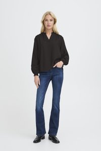 Blusa nera a maniche lunghe con scollo a V, spalle arricciate e polsini elasticizzati, abbinata a jeans aderenti blu scuro e stivaletti neri alla caviglia.