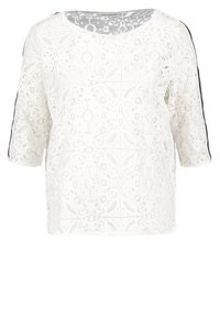 Blusa bianca in pizzo con scollatura rotonda, maniche a tre quarti e dettagli neri ai lati. Motivo in pizzo intricato su tutta la superficie. Texture morbida.