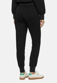 Pantaloni da jogging neri con una vestibilità affusolata, vita elastica e polsini. Abbinati a sneakers bianche con dettagli verdi.