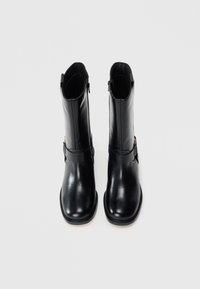 Bottines en cuir noir à finition lisse, dotées d'une fermeture éclair sur le côté, d'un bout arrondi et d'une sangle décorative autour de la tige.