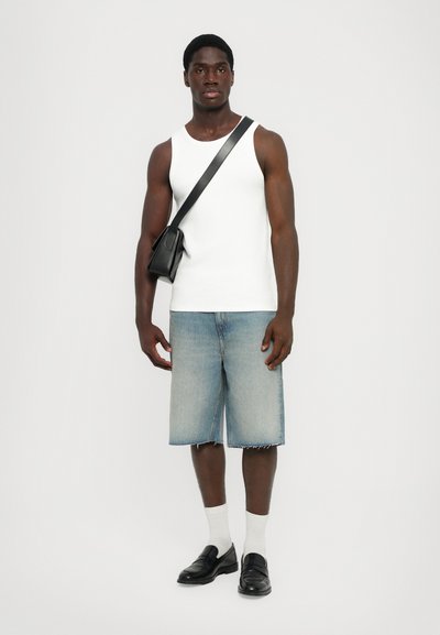 Un débardeur blanc sans manches, un short en denim bleu délavé, des mocassins noirs, des chaussettes blanches et un petit sac bandoulière noir. Tenue décontractée simple.