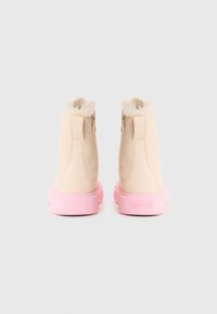 Beige ankelstøvler med rosa gummisåler og pelskledde innsider. Har glidelåser på siden for enkel påkledning. Glatt tekstur med avrundet form.