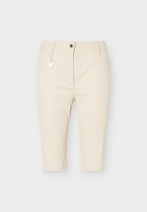 Beige knælange tætsiddende shorts med frontknap og lynlås, bæltestropper og en dekorativ sølvkæde på venstre side.