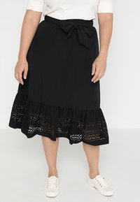 Svart kjol med lager-puffig fåll som har intrikata utskärningar. Materialet ser lätt och luftigt ut. Knytning vid midjan. I kombination med vita sneakers.