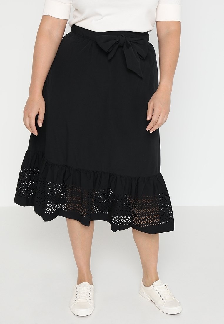 Svart kjol med lager-puffig fåll som har intrikata utskärningar. Materialet ser lätt och luftigt ut. Knytning vid midjan. I kombination med vita sneakers.