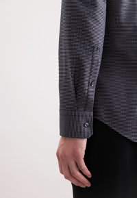 Donker-gepatenteerd shirt met een gestructureerde stof, knoopmanchetten en een getailleerde pasvorm. De kleur is overwegend navy met een geometrisch ontwerp.