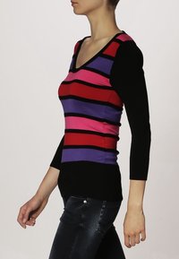 Pruhovaný svetr s fialovými, červenými a růžovými vodorovnými pruhy na černém pozadí. Výstřih do V a tříčtvrteční rukávy. Standardní střih.