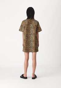 Lyhyestä, pehmeästä kankaasta valmistettu leopardi-kuosisessa mekko; siinä on löysä cut ja lyhyet hihat. Yhdistetty mustiin sandaaleihin. Takakatsaus esitetty.