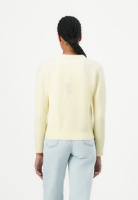 Maglione giallo vaporoso con scollatura rotonda e polsini a coste. Indossato con jeans azzurri chiari, che mostrano un design casual e aderente. Vista posteriore esposta.