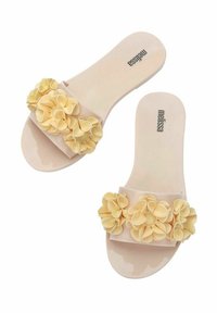 Sandalias de slide rosas hechas de un material brillante, con una banda adornada con acentos florales amarillos texturizados. Decoradas con múltiples pétalos superpuestos.