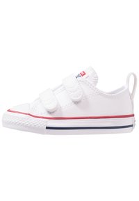 Valge kanvasest sneaker, millel on kaks Velcro riivi, kontrastne punane äär ja tumesinised aktsendid tallal; ümar varvas ja kummist välistald.