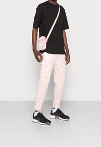 Svart t-shirt, ljusrosa mjukisbyxor med sidfickor, svarta träningsskor och en liten rosa axelväska. Enkel och funktionell design.