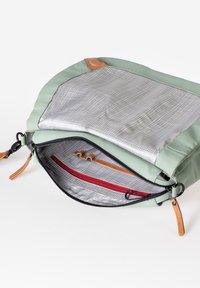 Borsa in tessuto verde con apertura con zip, dotata di un interno a motivo a griglia, dettagli rossi e beige e particolari in pelle. L'interno include tasche.