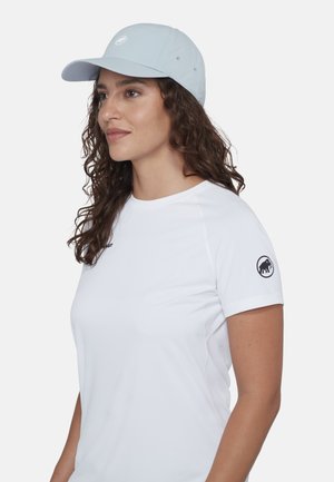 Kvinde med krøllet hår iført en lyseblå kasket og hvid T-shirt med korte ærmer med mammutlogo på ærmet, vendt mod venstre.