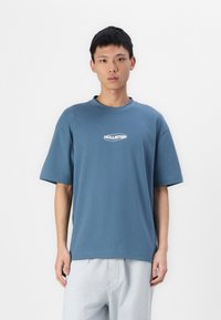 Kék, oversized póló rövid ujjal, kerek nyakkivágással, középen fehér "Hollister" logóval. Puha pamutból készült.