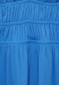 Tissu bleu avec des sections froncées par des bandes élastiques, affichant une texture lisse et une couleur uniforme. Des rangées de fronces créent de la dimension.