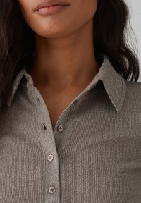 Geripptes, metallisches Strickhemd in sanftem Taupe mit Kragen, das über Knopfverschlüsse verfügt und eine subtile schimmernde Textur aufweist.