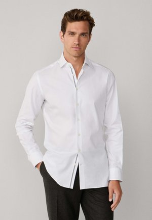 Witte katoenen overhemd met klassieke kraag, lange mouwen en een achterpanddetail; aangevuld met subtiele contrasterende stiksels.