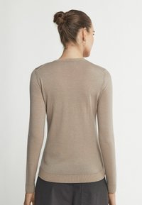 Sweter dzianinowy w kolorze beżowym, z długimi rękawami i okrągłym dekoltem. Tkanina ma gładką teksturę z prążkowanymi akcentami na mankietach i u dołu.